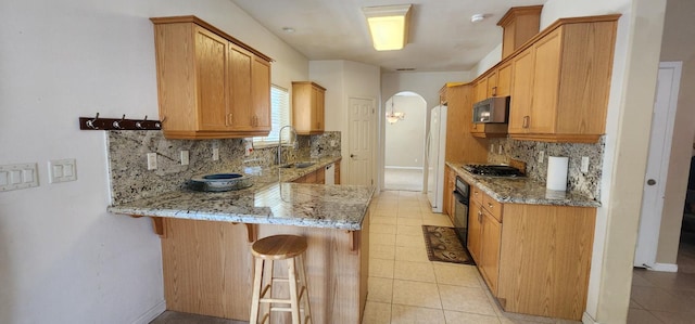 5360 E Heaton Ave, Fresno, CA 93727 - kitchen featuring freestanding refrigerator, arched walkways, light stone countertops, black oven, and a peninsula