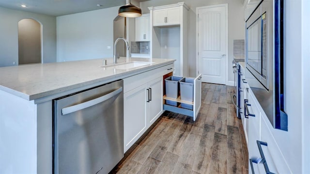 kitchen featuring stainless steel dishwasher, wood finished floors, a sink, light stone counters, and white cabinets