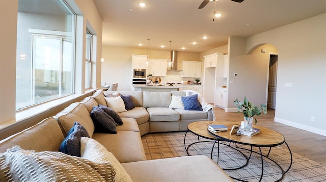 living room featuring a ceiling fan, light wood-style floors, baseboards, recessed lighting, and arched walkways
