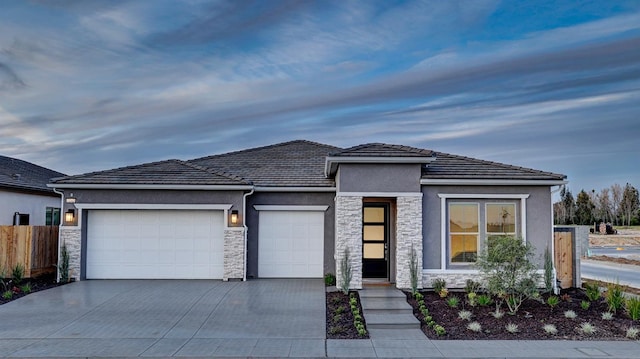 prairie-style home featuring fence, stone siding, a garage, stucco siding, and driveway