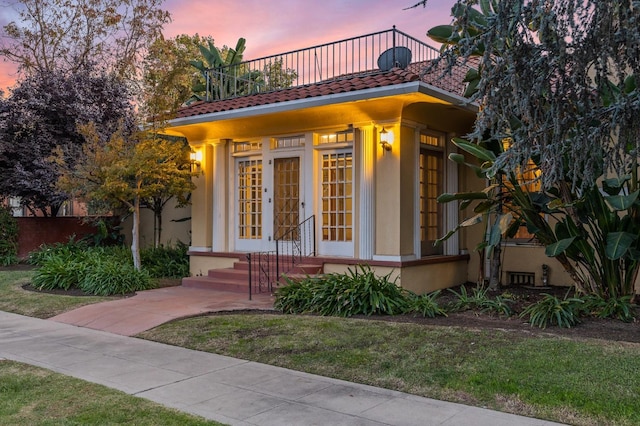 2436 N Van Ness Blvd, Fresno, CA 93704 - exterior entry at dusk featuring a lawn, a tiled roof, stucco siding, and a balcony