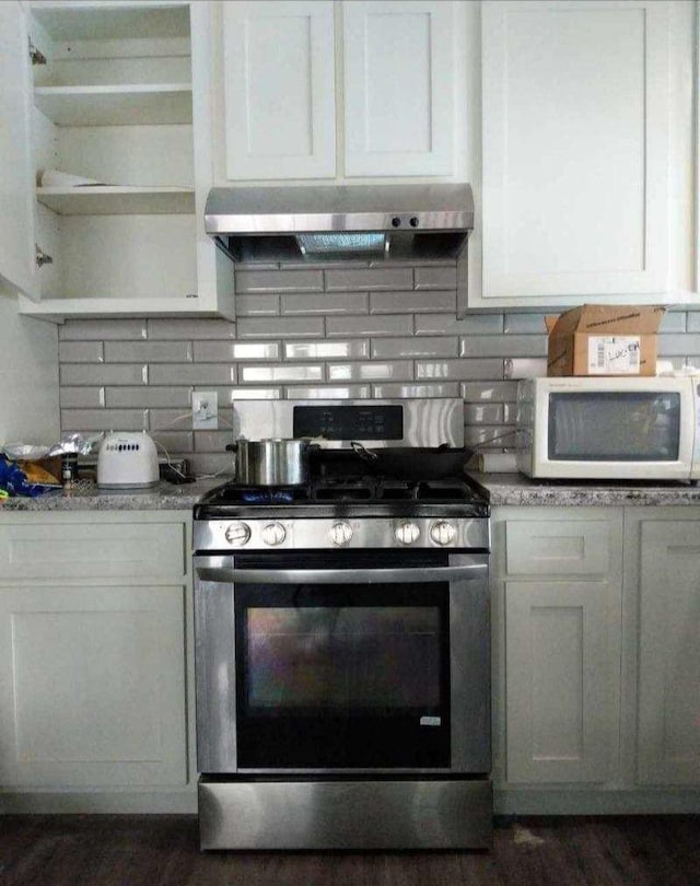 kitchen with decorative backsplash, open shelves, gas stove, white microwave, and under cabinet range hood