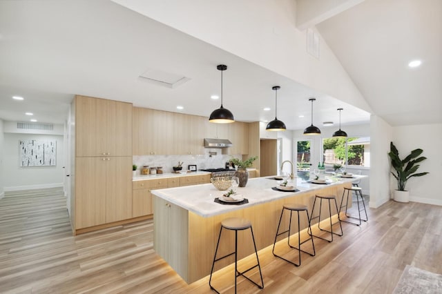 2044 W San Bruno Ave, Fresno, CA 93711 - kitchen with light brown cabinetry, a kitchen breakfast bar, baseboards, under cabinet range hood, and modern cabinets