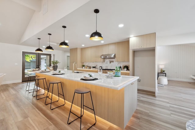 2044 W San Bruno Ave, Fresno, CA 93711 - kitchen with under cabinet range hood, light brown cabinetry, a breakfast bar, and modern cabinets