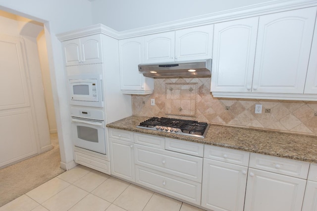 kitchen featuring white appliances, tasteful backsplash, light stone counters, under cabinet range hood, and white cabinetry
