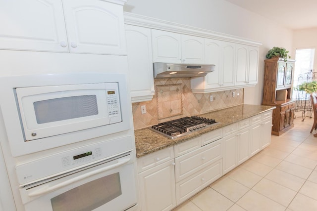 kitchen featuring backsplash, white appliances, light stone counters, and under cabinet range hood