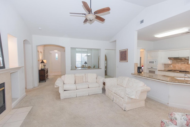 living room with ceiling fan with notable chandelier, vaulted ceiling, arched walkways, light carpet, and a fireplace