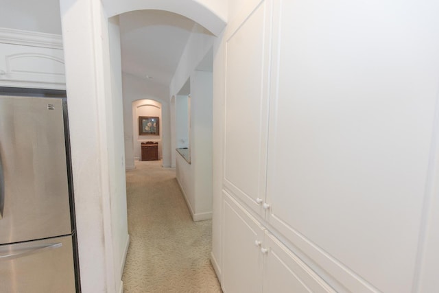 corridor featuring arched walkways, baseboards, and light colored carpet
