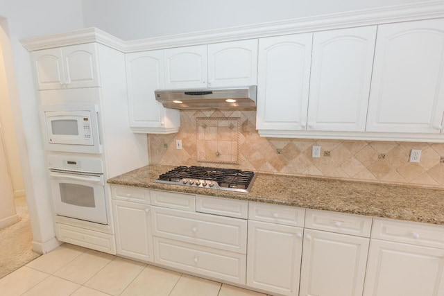 kitchen with under cabinet range hood, backsplash, light stone countertops, and white appliances