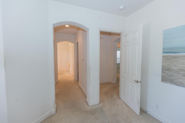 corridor featuring light carpet, arched walkways, and baseboards