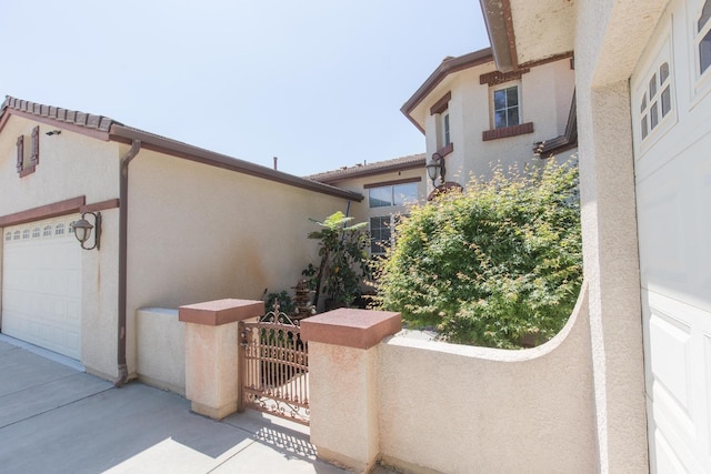 view of home's exterior featuring driveway, stucco siding, a gate, and an attached garage