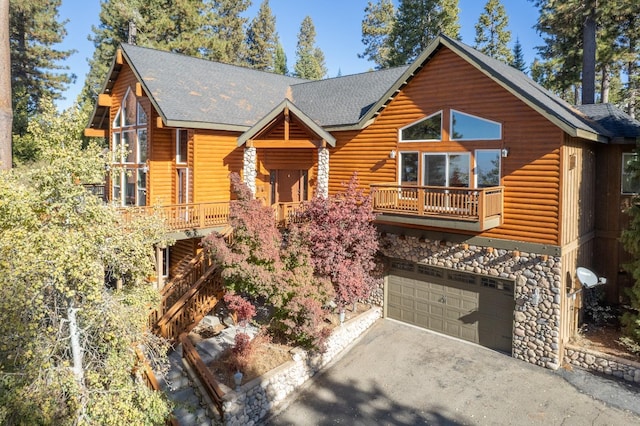 rustic home featuring stone siding, an attached garage, a shingled roof, a balcony, and driveway