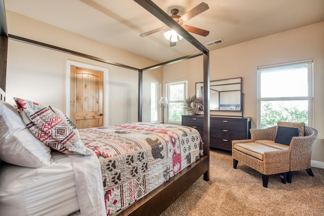 carpeted bedroom featuring multiple windows, visible vents, and ceiling fan