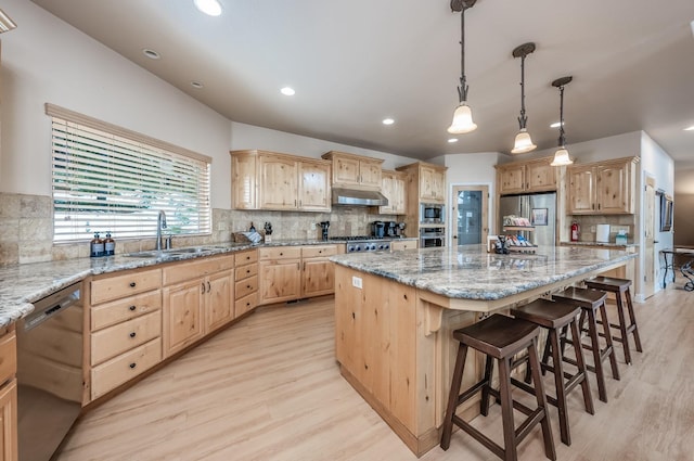 kitchen with a sink, stainless steel appliances, light wood-style flooring, light brown cabinetry, and a center island