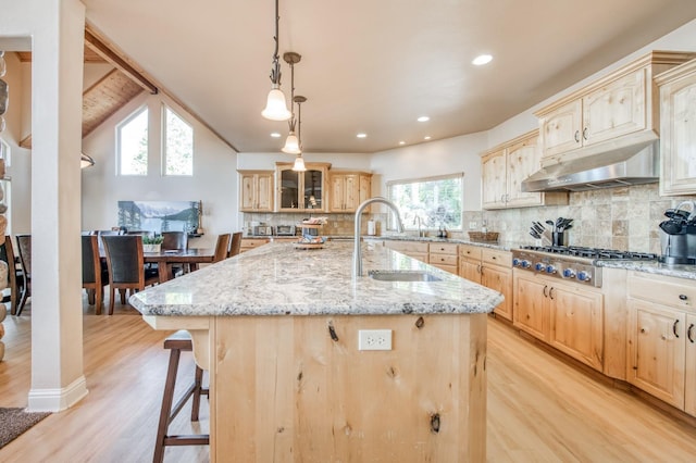 kitchen with light brown cabinetry, a kitchen breakfast bar, under cabinet range hood, light wood-style floors, and stainless steel gas cooktop