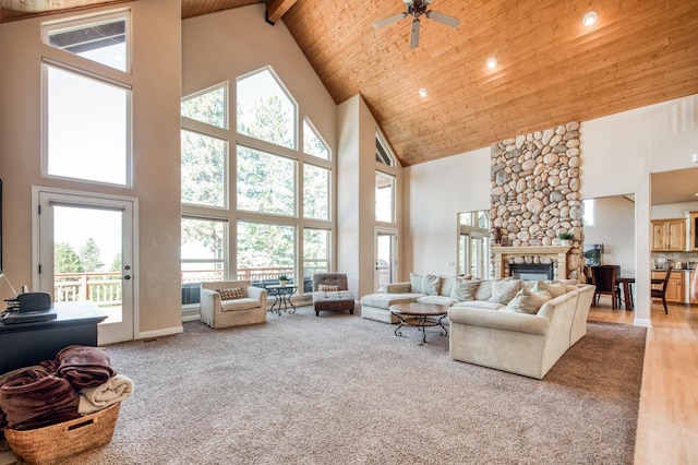living area with a ceiling fan, a stone fireplace, a healthy amount of sunlight, and high vaulted ceiling
