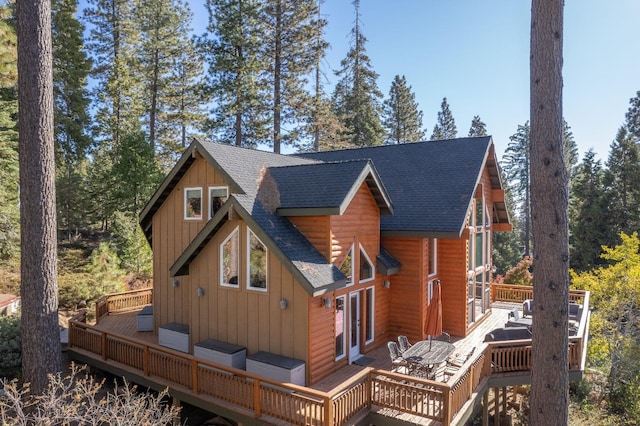 rear view of house with a deck, outdoor dining space, roof with shingles, and board and batten siding