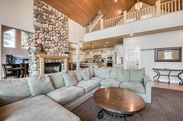 living room featuring wooden ceiling, a stone fireplace, a wealth of natural light, and high vaulted ceiling