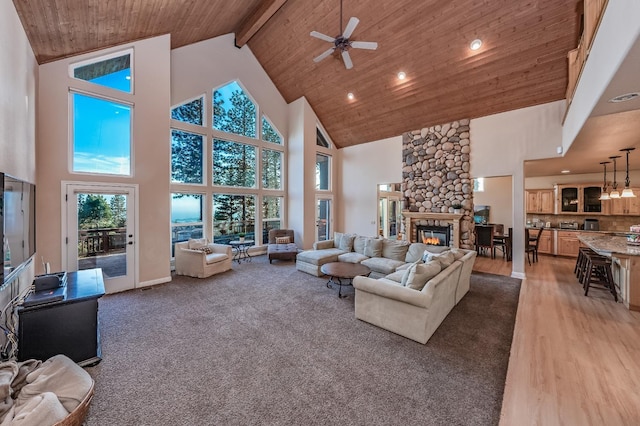 living area featuring wooden ceiling, a ceiling fan, a stone fireplace, and high vaulted ceiling