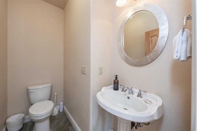 half bathroom with toilet, baseboards, and a sink