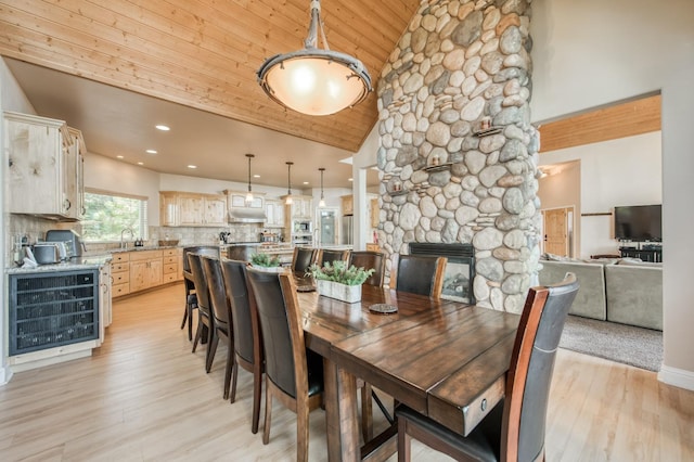 dining room with high vaulted ceiling, wooden ceiling, light wood finished floors, a fireplace, and beverage cooler
