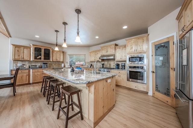 kitchen featuring light wood finished floors, stainless steel appliances, light brown cabinetry, and under cabinet range hood