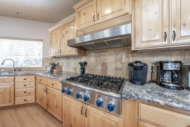 kitchen featuring a sink, light brown cabinetry, under cabinet range hood, light stone counters, and stainless steel gas cooktop