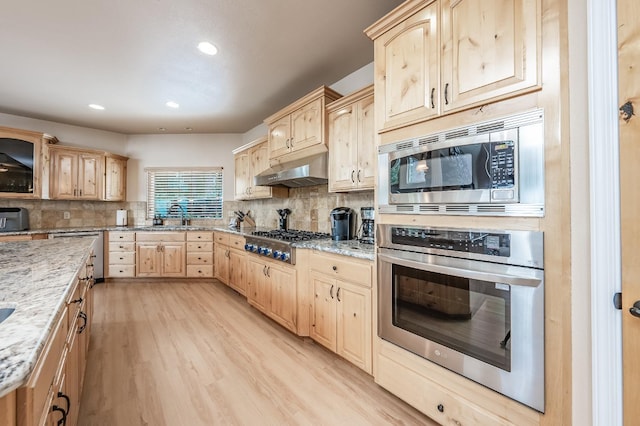 kitchen featuring a sink, stainless steel appliances, light stone counters, under cabinet range hood, and light brown cabinetry