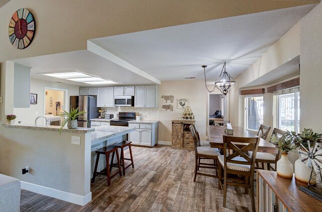 20794 E Weldon Ave, Sanger, CA 93657 - kitchen with stainless steel appliances, wood finished floors, a peninsula, a breakfast bar, and a chandelier