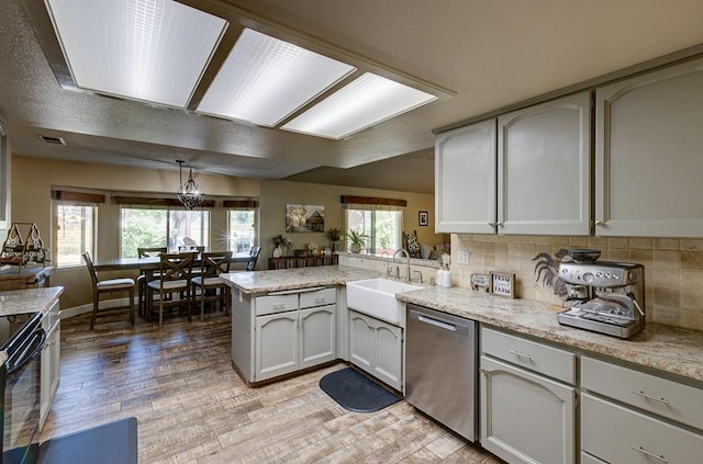 kitchen featuring a sink, a peninsula, light wood-type flooring, decorative backsplash, and stainless steel dishwasher