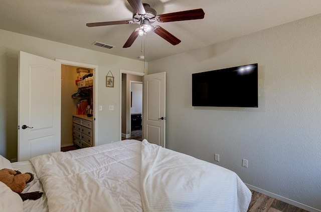 bedroom with wood finished floors, a ceiling fan, visible vents, baseboards, and a spacious closet