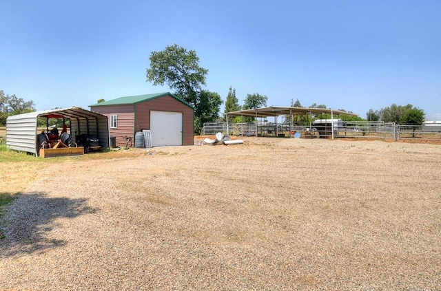 view of yard with a detached carport, an outdoor structure, a detached garage, fence, and dirt driveway