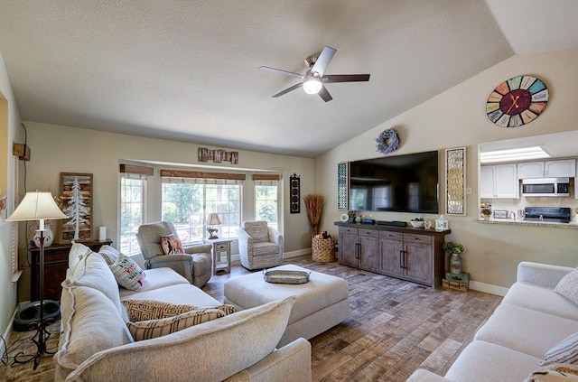 living area featuring lofted ceiling, a textured ceiling, baseboards, ceiling fan, and wood finished floors