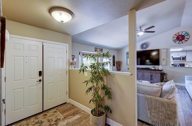 entryway featuring lofted ceiling, wood finished floors, a textured ceiling, a ceiling fan, and baseboards