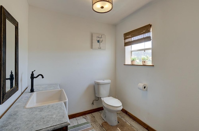 half bathroom with toilet, baseboards, vanity, and wood finished floors