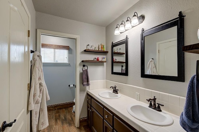 full bathroom with a sink, double vanity, backsplash, and wood finished floors