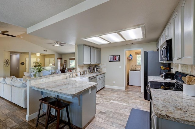 kitchen with washer / clothes dryer, a breakfast bar area, ceiling fan, a peninsula, and appliances with stainless steel finishes