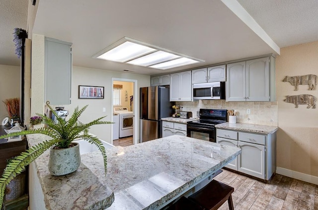 kitchen featuring light wood finished floors, baseboards, backsplash, appliances with stainless steel finishes, and washer / clothes dryer