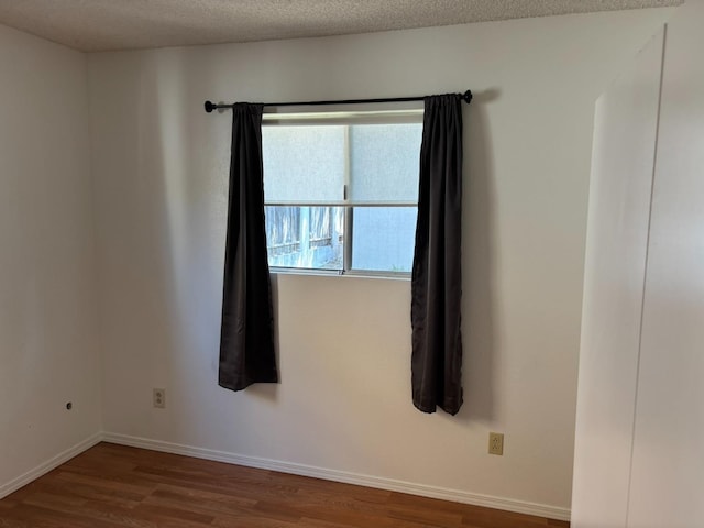 empty room featuring a textured ceiling, baseboards, and wood finished floors