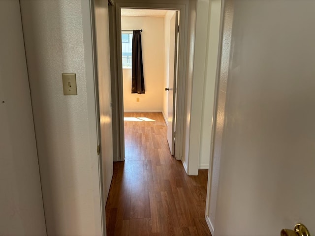 corridor with a textured wall, baseboards, and dark wood finished floors