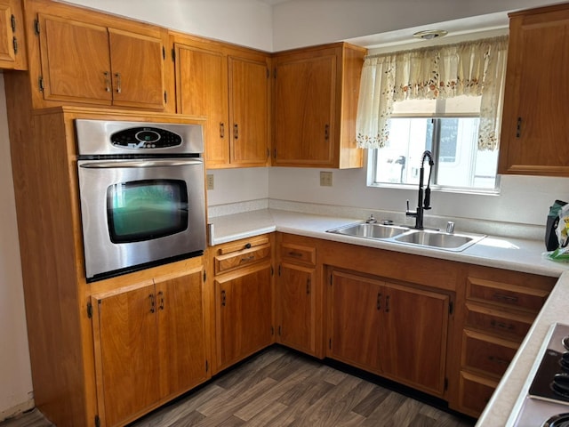 kitchen featuring brown cabinetry, oven, a sink, light countertops, and dark wood-style floors