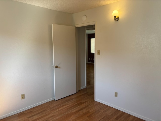 unfurnished room featuring baseboards, a textured ceiling, and wood finished floors