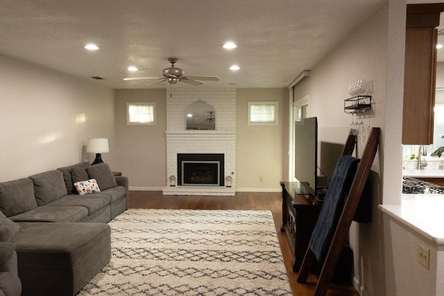 living area featuring ceiling fan, a brick fireplace, plenty of natural light, and dark wood-style flooring