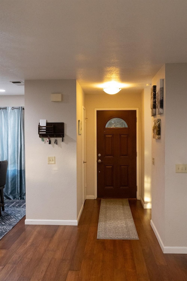 foyer with baseboards, visible vents, and dark wood-style floors