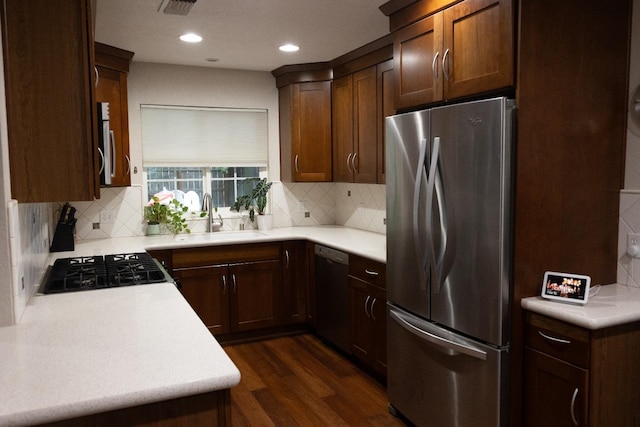 kitchen with stainless steel appliances, a sink, decorative backsplash, dark wood-type flooring, and light countertops