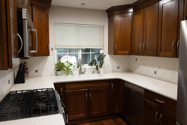 kitchen with a sink, tasteful backsplash, dark wood finished floors, light countertops, and appliances with stainless steel finishes