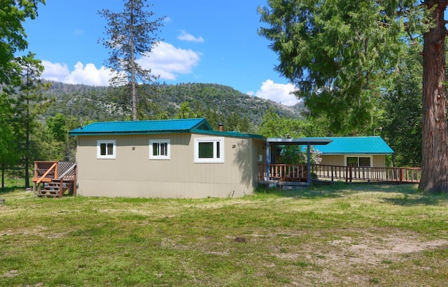 rear view of property featuring a forest view, a yard, and a deck with mountain view