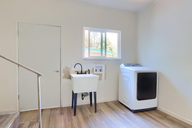 clothes washing area featuring laundry area, light wood finished floors, baseboards, and washer / dryer