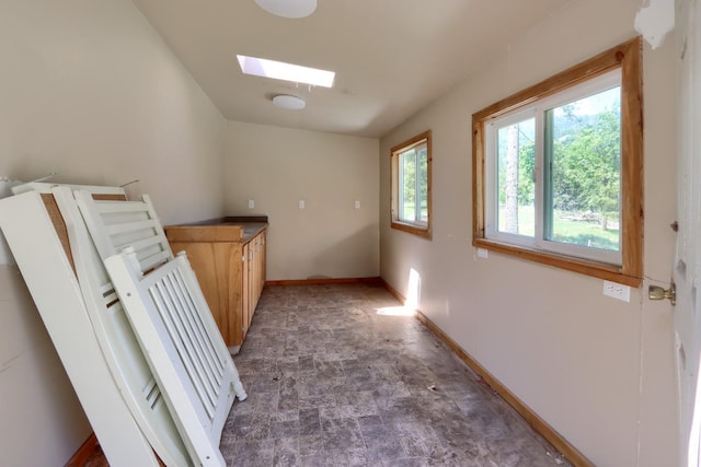 hall featuring a skylight, baseboards, and stone finish flooring