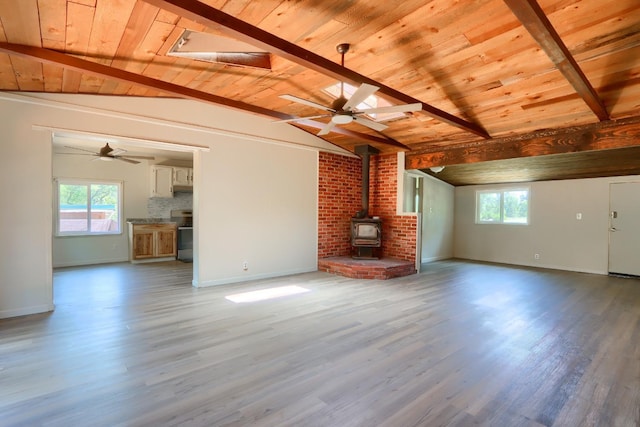 unfurnished living room featuring wooden ceiling, a wood stove, a wealth of natural light, and vaulted ceiling with beams
